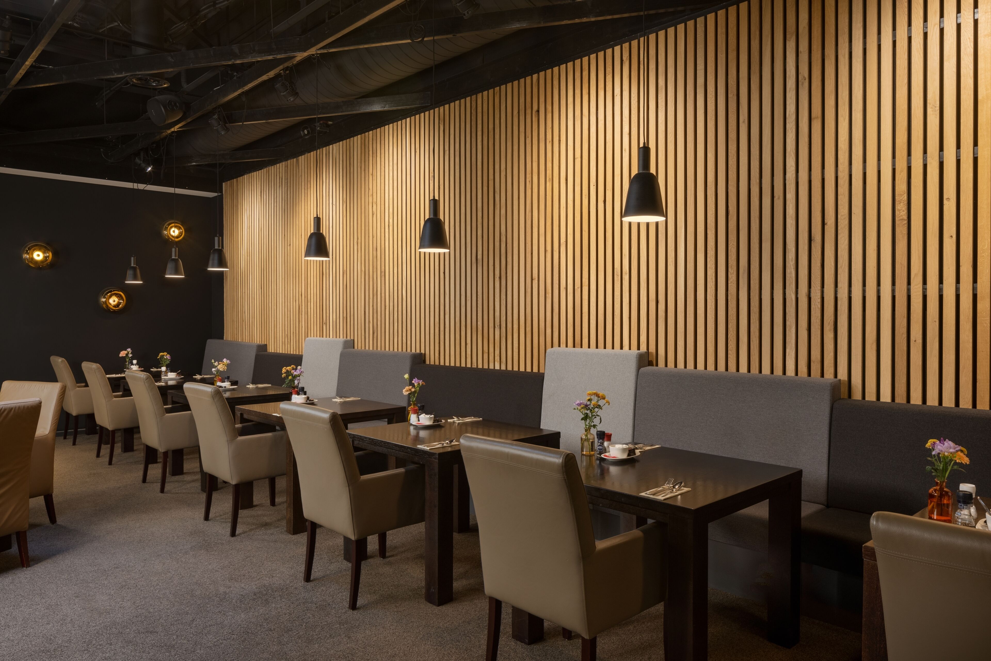 A modern dining area with wooden panel walls, black pendant lights, and leather chairs.