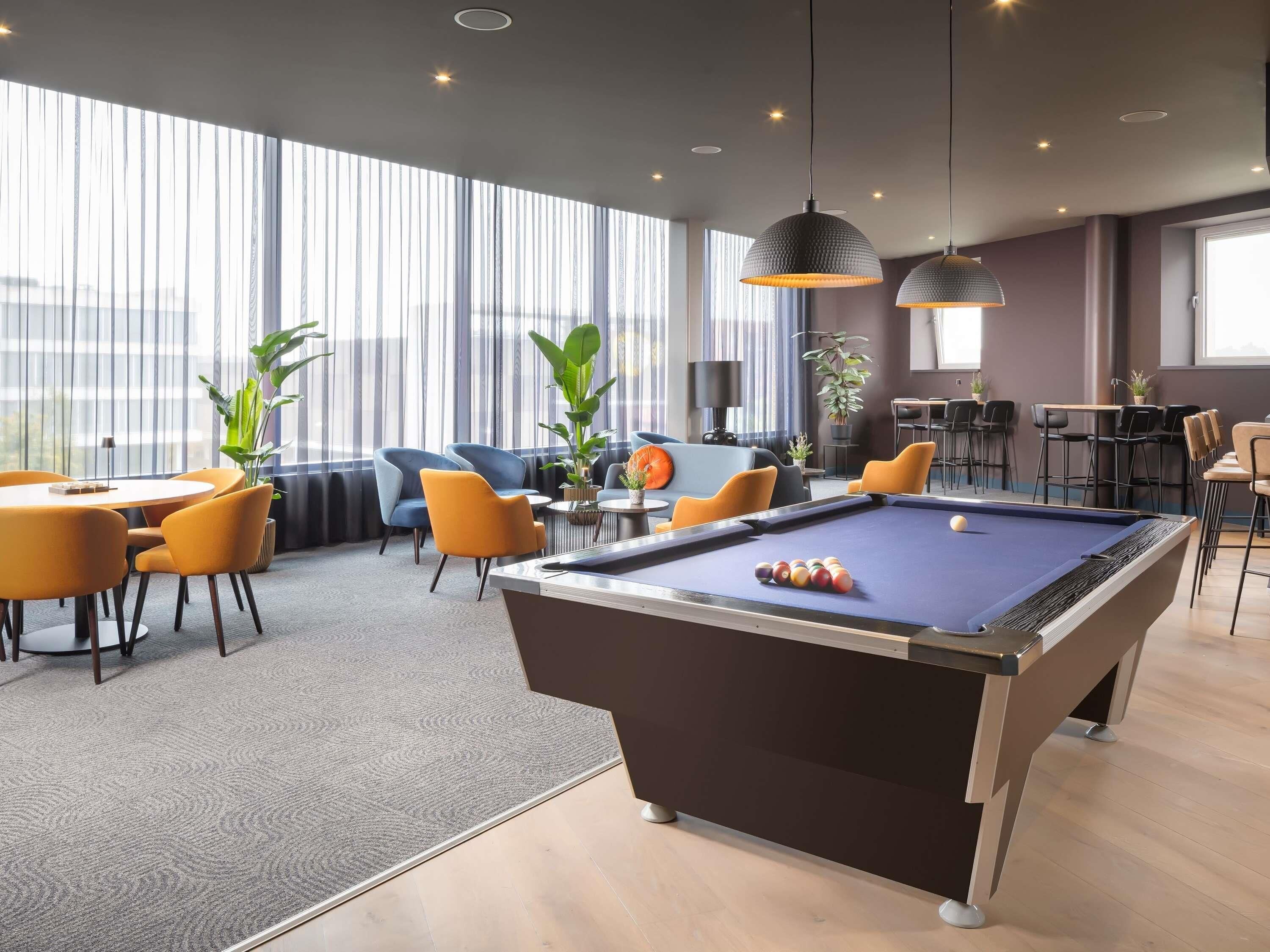 A modern lounge area with a pool table, seating, and large windows.
