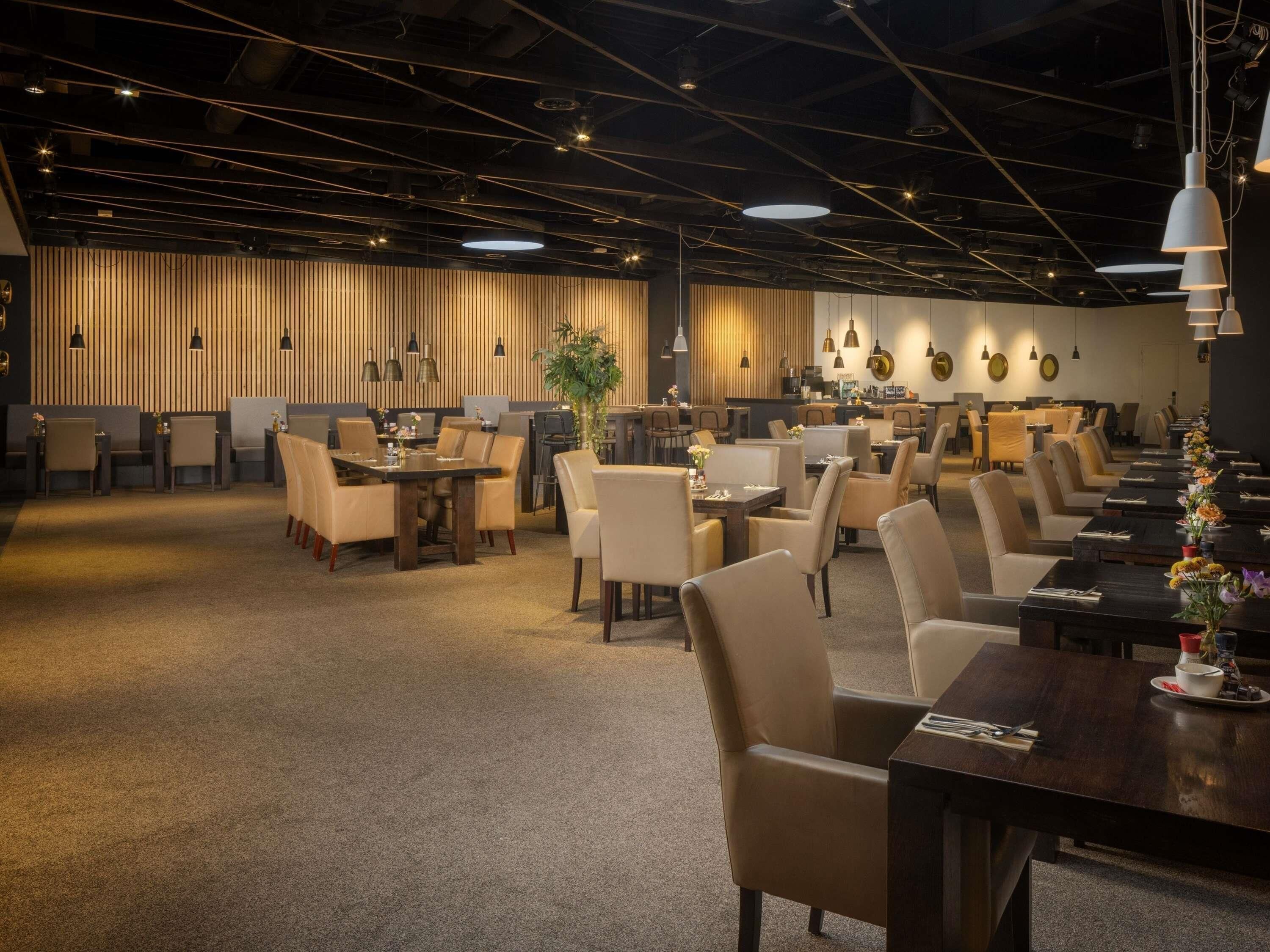 A spacious dining area with multiple tables and chairs, a high ceiling with exposed beams, and pendant lighting.