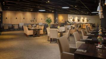 A spacious dining area with multiple tables and chairs, a high ceiling with exposed beams, and pendant lighting.