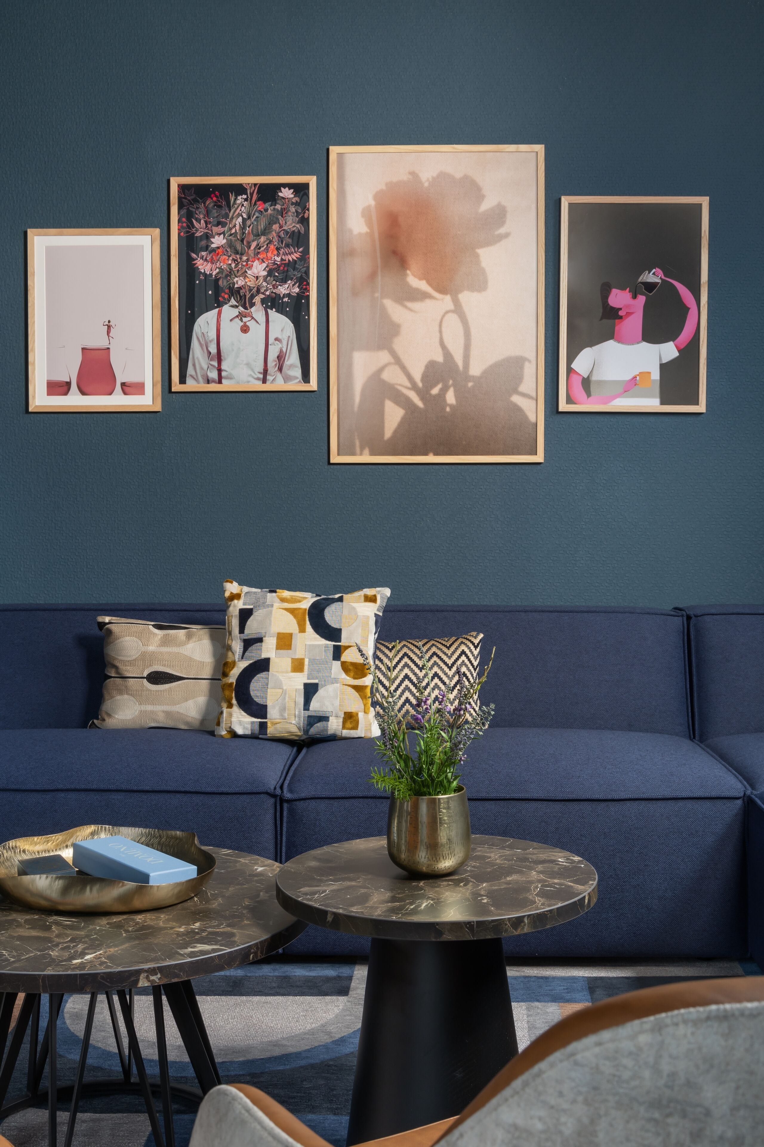 Un salon moderne avec un canapé bleu, une table basse ronde et des œuvres d’art encadrées accrochées au mur.