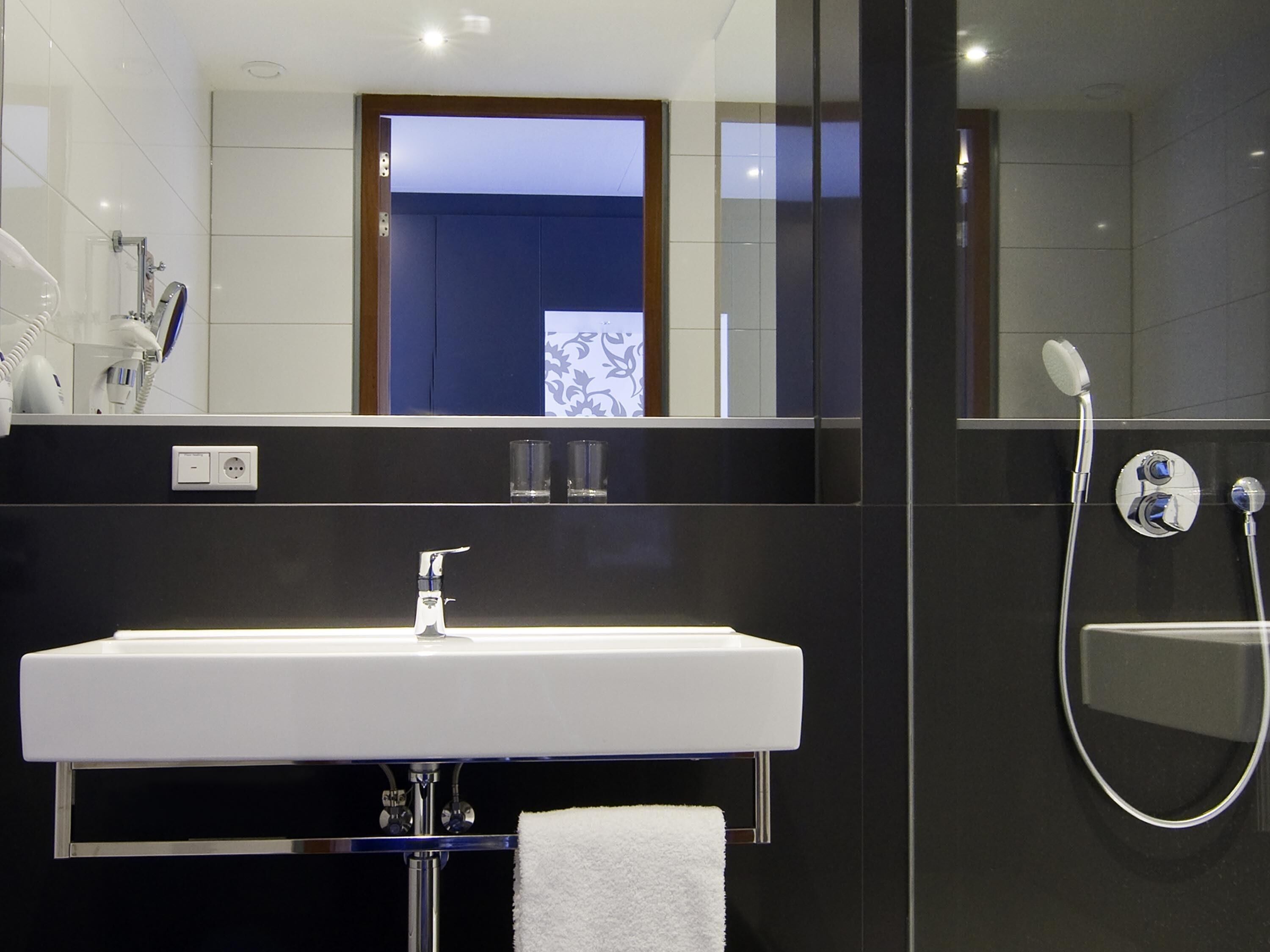 A modern bathroom with a white sink, a mirror, and a shower.