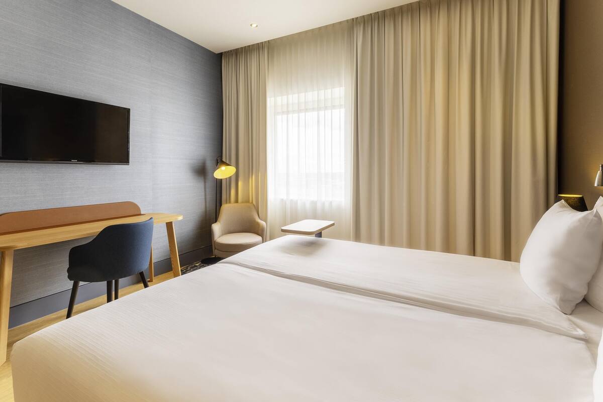 A hotel room with a bed, a desk, a chair, a TV, and a lamp.