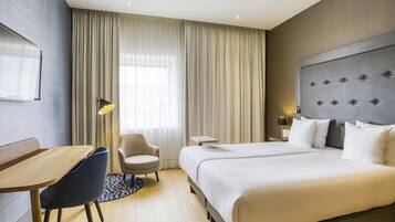Una habitación de hotel con una cama grande, un escritorio, una silla, una mesita y una lámpara.