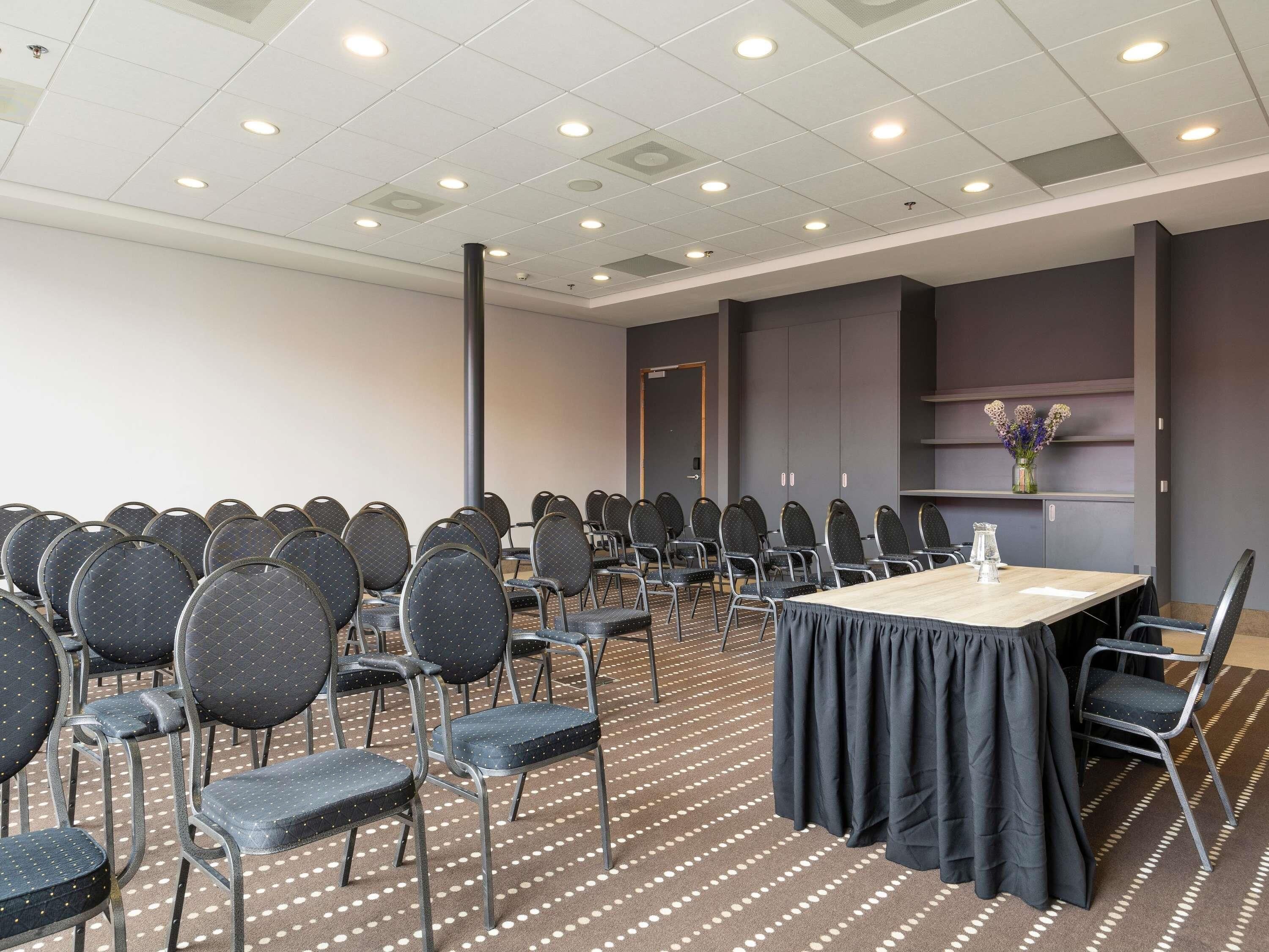 A conference room with a long table and rows of chairs, a patterned carpet, and a ceiling with recessed lighting.