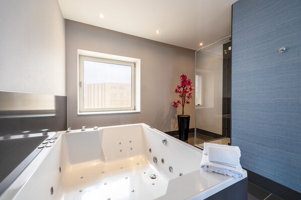 A modern bathroom with a large bathtub, a window, and a potted plant.