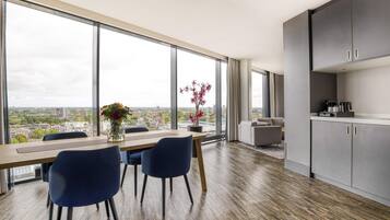 Een moderne keuken met een groot raam, een eethoek met een tafel en stoelen, en uitzicht op een stadsgezicht.
