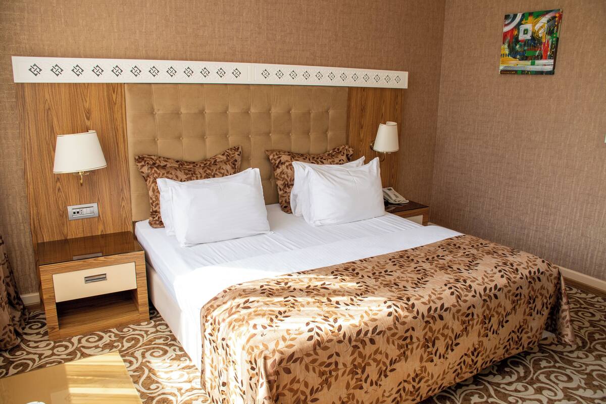 A hotel room with a tufted headboard, a bed with white linens, a leopard print throw, and two bedside tables with lamps.