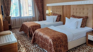 Habitación de hotel con dos camas, un ventanal con cortinas, alfombra estampada y cabecero de madera.