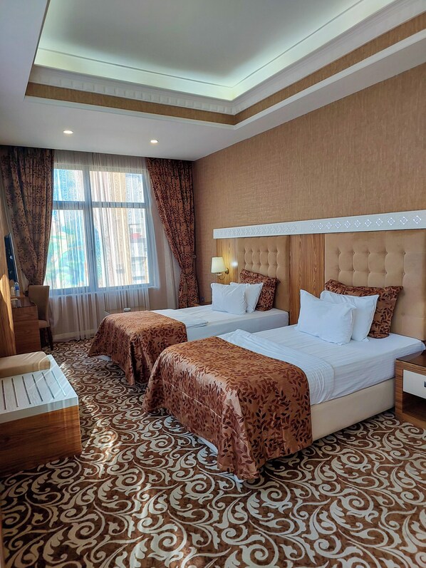 Une chambre d’hôtel avec deux lits, une grande fenêtre avec des rideaux, une moquette à motifs et une tête de lit en bois.