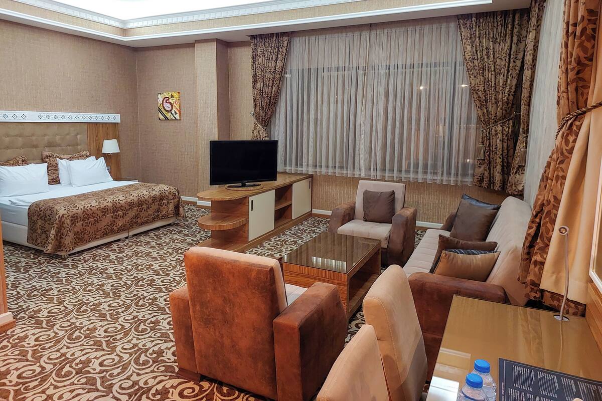A hotel room with a bed, a sofa, a TV on a wooden stand, and a coffee table.