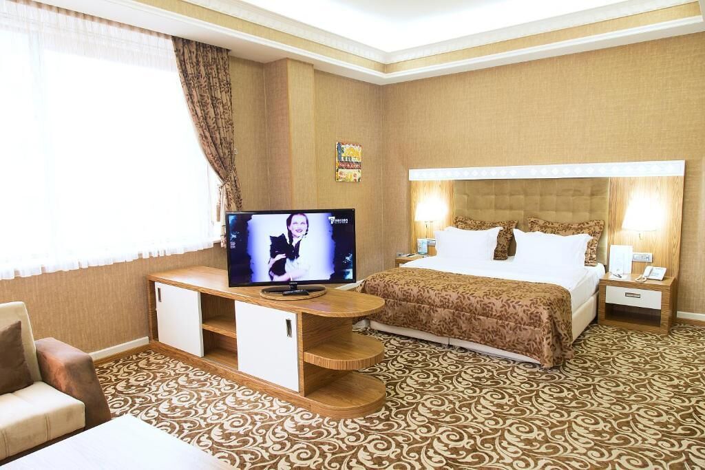A hotel room with a bed, a TV on a wooden stand, a bedside table, and a patterned carpet.