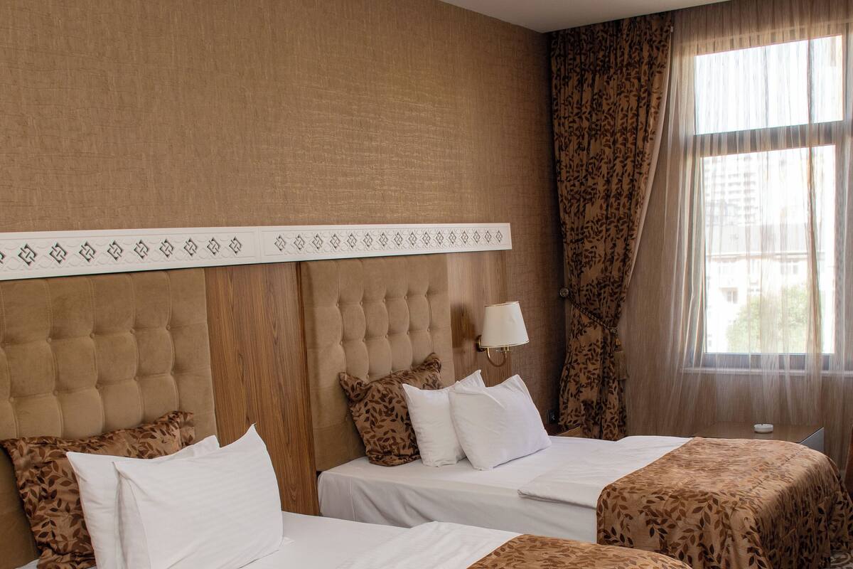 A hotel room with two beds, a patterned carpet, and a large window with curtains.