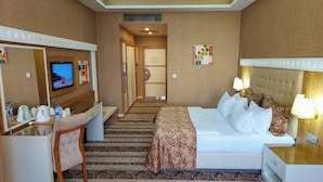 Habitación de hotel con cama, mesita de noche, lámpara, escritorio con silla, televisor y alfombra estampada.