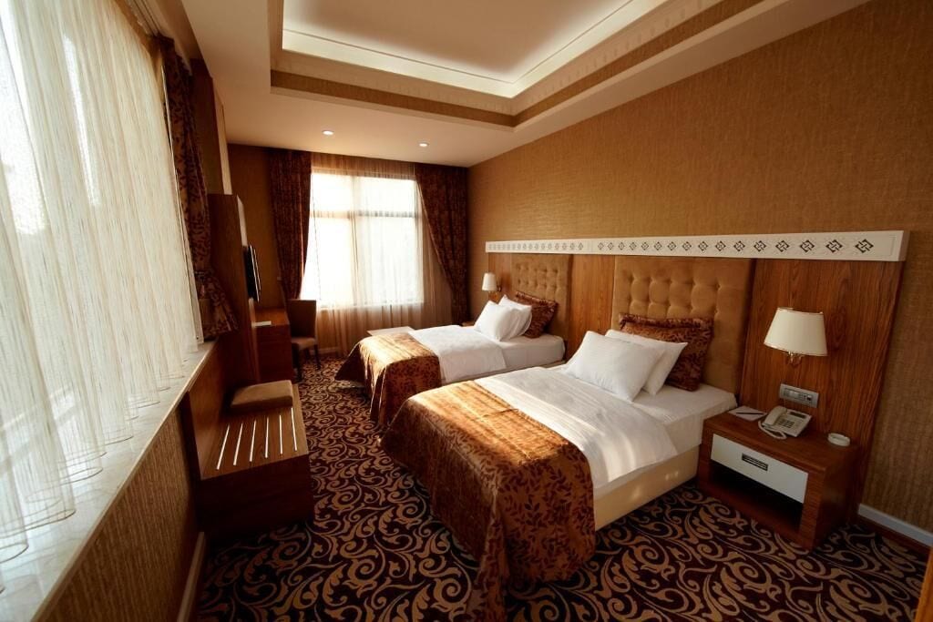 A hotel room with two beds, a desk, a chair, a TV, and a window with curtains.