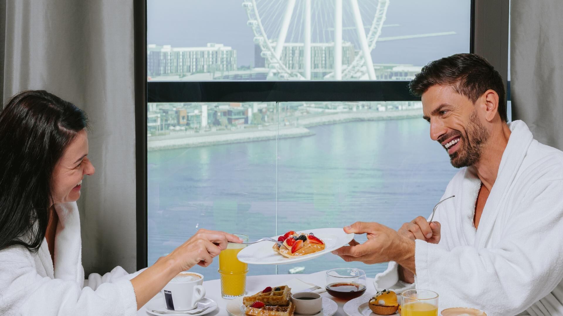 Un desayuno con vista a la ciudad, que incluye una noria grande y una mesa con diversas opciones para el desayuno.