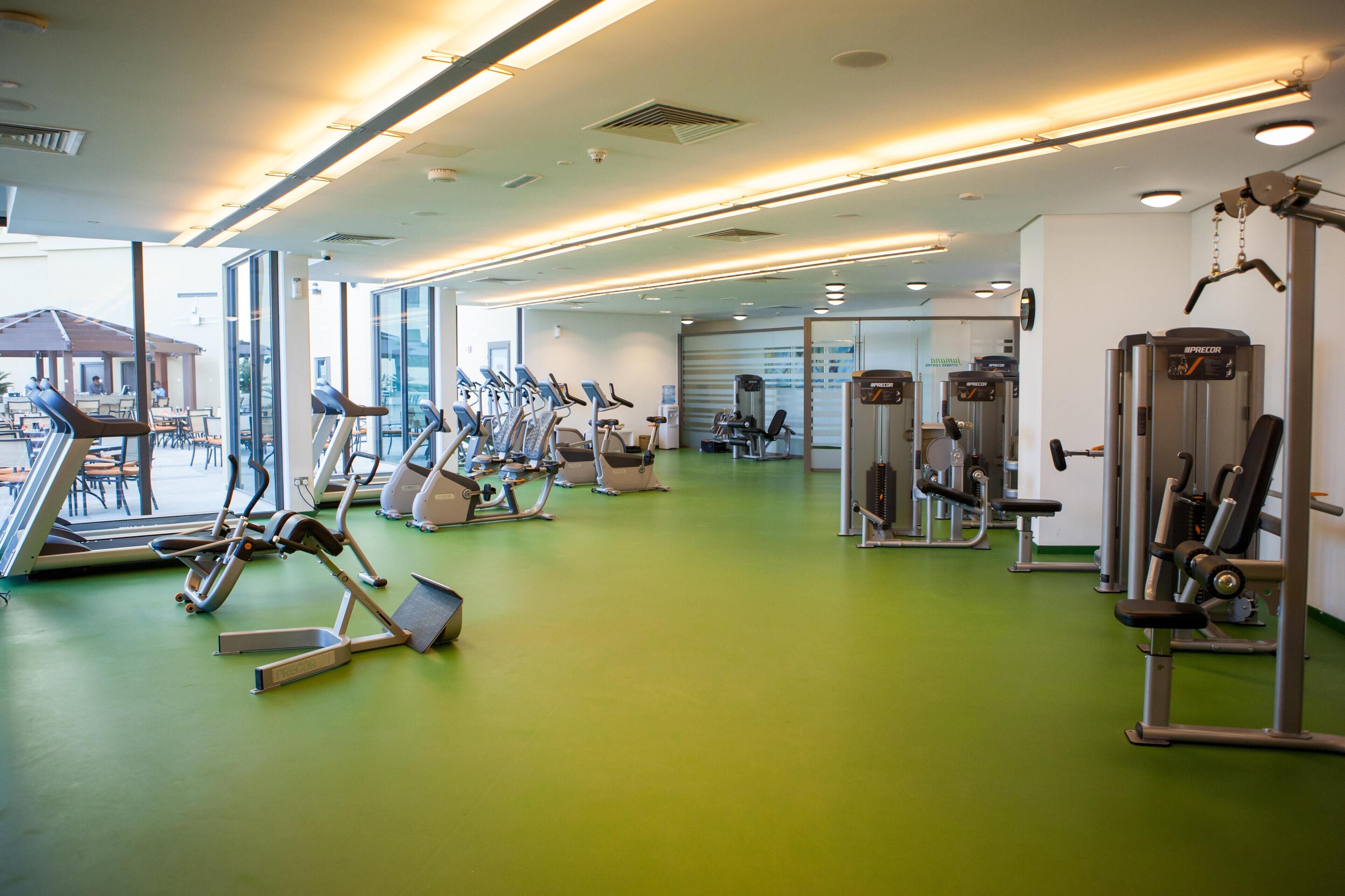 A gym with various exercise equipment, including treadmills and weight machines, and a green floor.