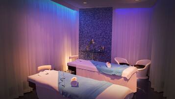 Relax in a serene spa room with two treatment beds, a shelf with amenities, and a clean, minimalist design.