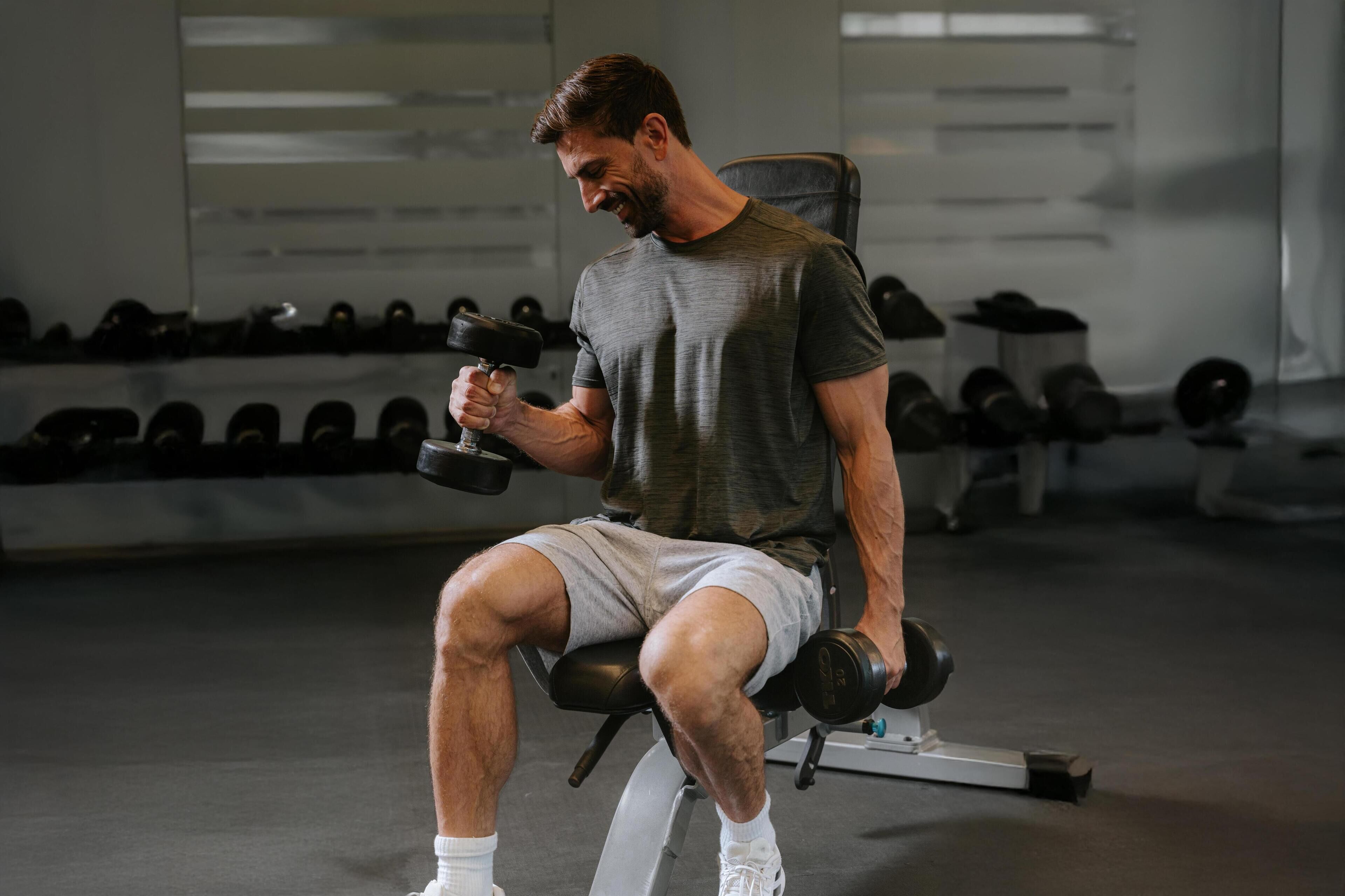 A man seated on a bench in a gym, holding dumbbells.