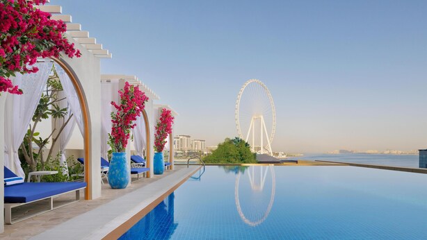 A pool area with lounge chairs and a view of a Ferris wheel. - JA Ocean View Hotel, Jumeirah Beach Dubai (Dubai)