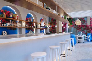 A bar area with white stools, shelves with bottles, and decorative plants.