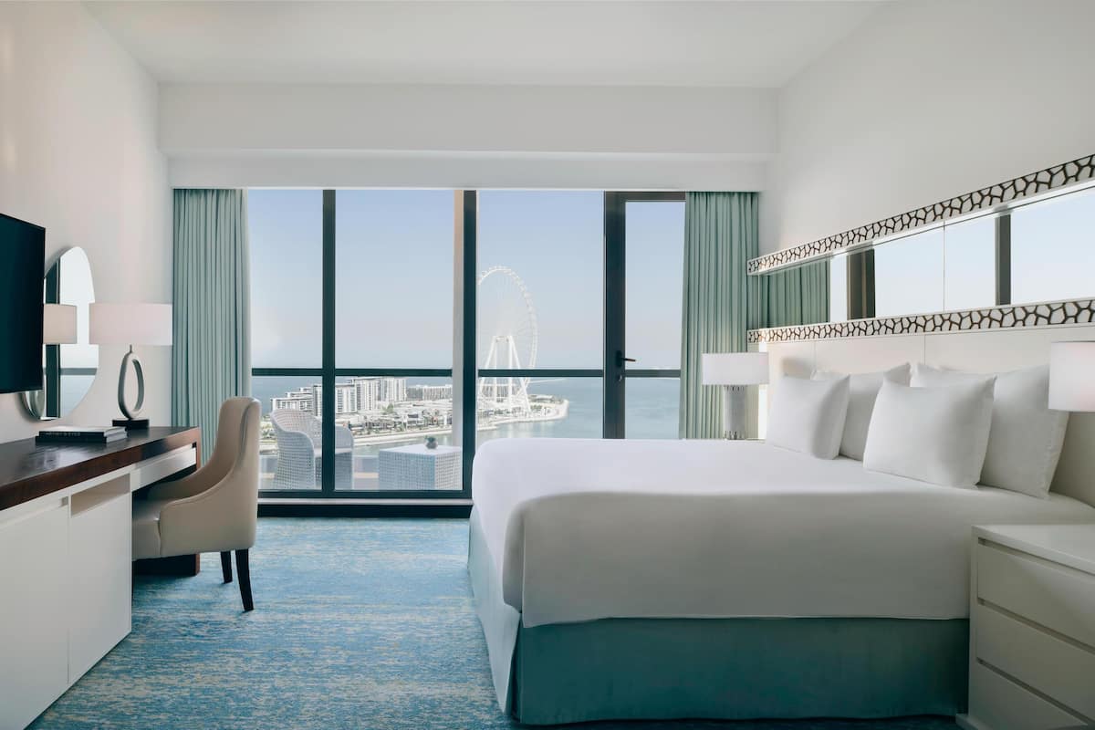 A hotel room with a large bed, a desk, and a view of a Ferris wheel and marina.