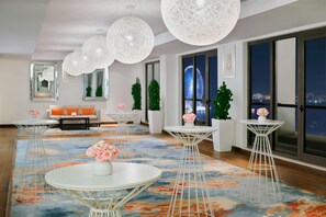 A modern hotel lobby with round tables, white pendant lights, and a colorful carpet.