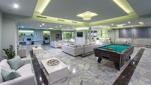 A modern living room with a pool table, sofas, and a dining area.