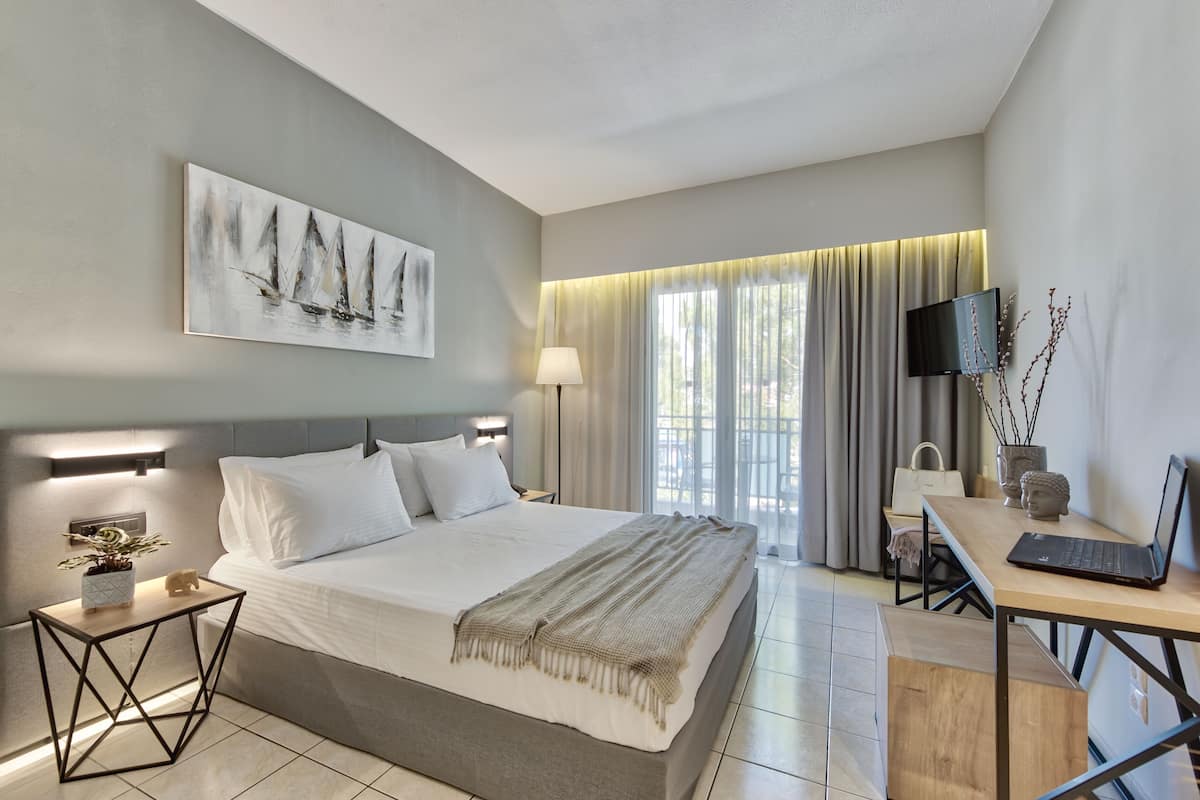 Habitación de hotel moderna con una cama grande, mesitas de noche, un escritorio con una computadora portátil, un televisor y un cuadro en la pared.