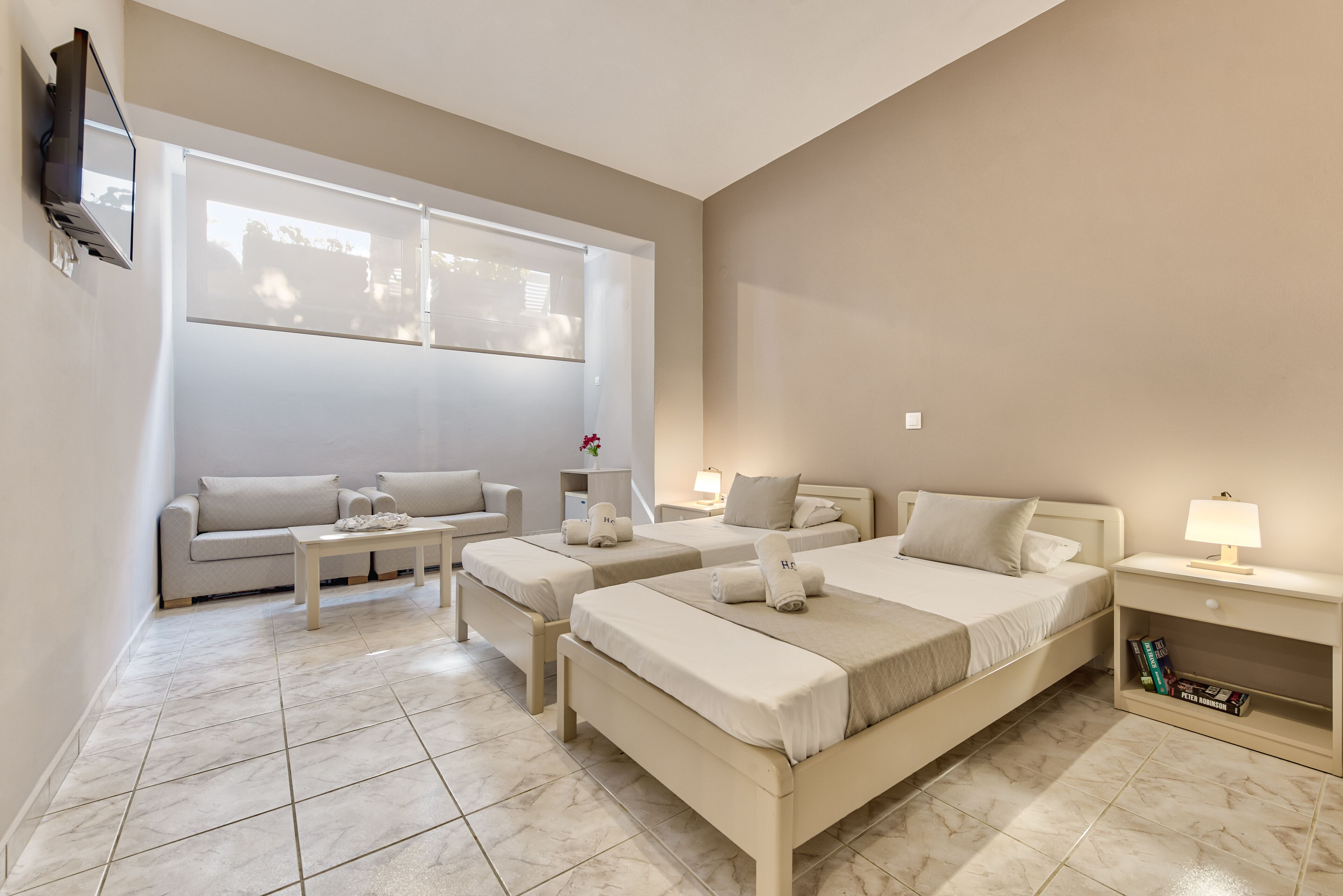 A hotel room with two beds, a sofa, a coffee table, and a TV mounted on the wall.