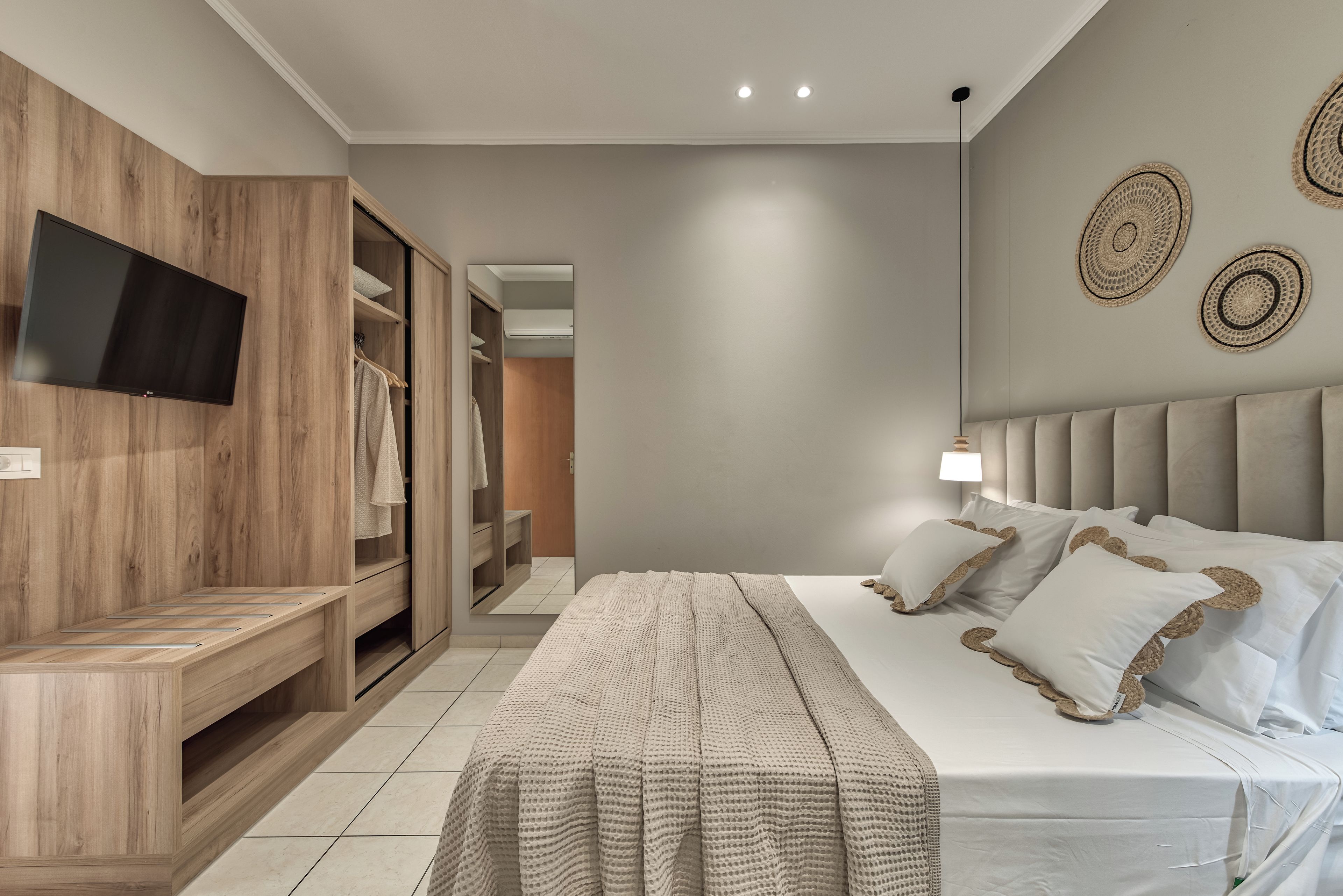 A modern bedroom with a large bed, a TV mounted on a wooden panel, a wardrobe, and a bedside table.