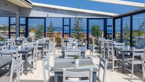 A rooftop terrace with tables and chairs, overlooking a coastal landscape.