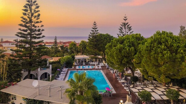 A resort with a swimming pool, lounge chairs, and a view of the sea at sunset.