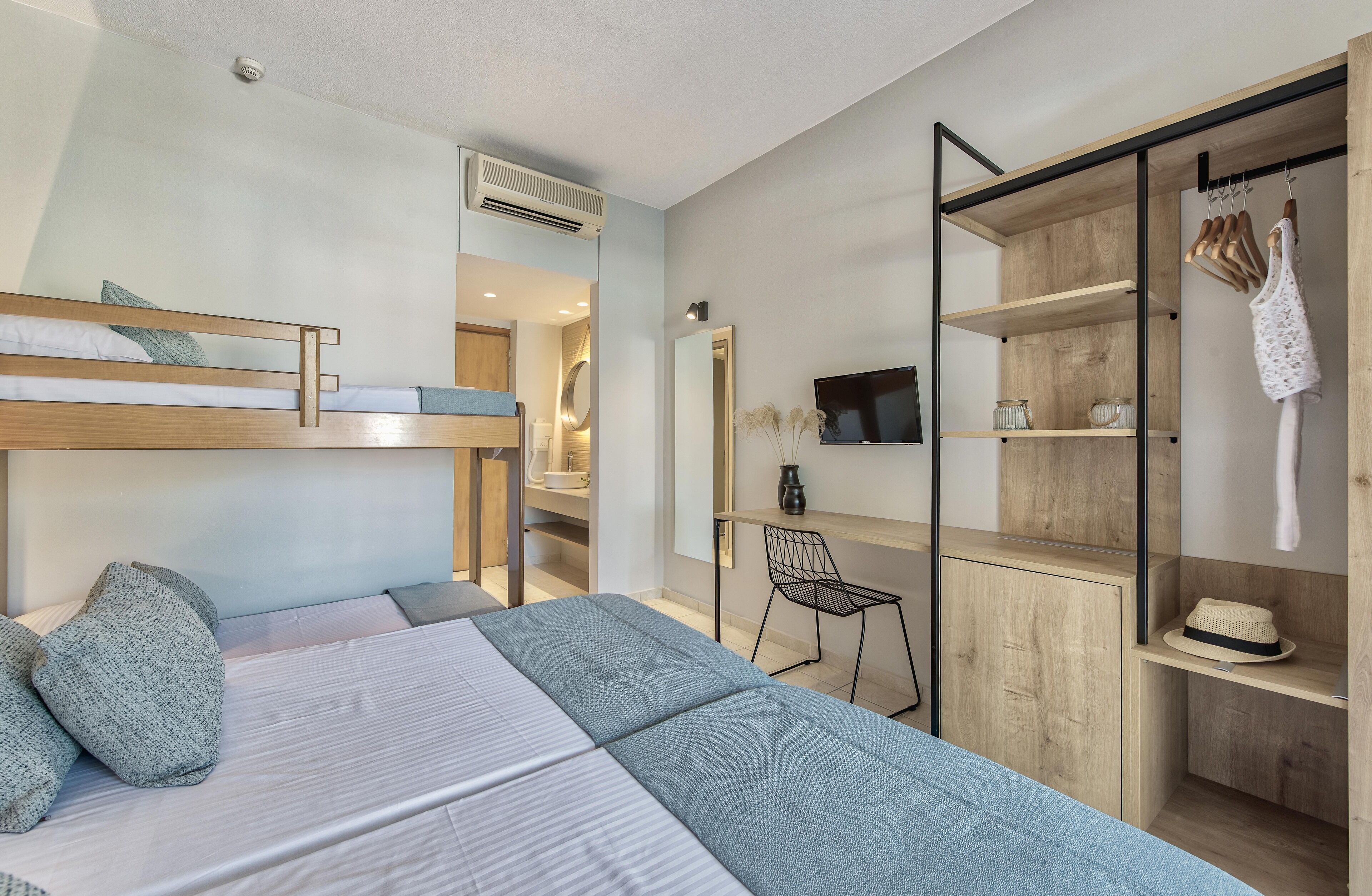 A modern hotel room with a bunk bed, a desk, a chair, and a wardrobe.