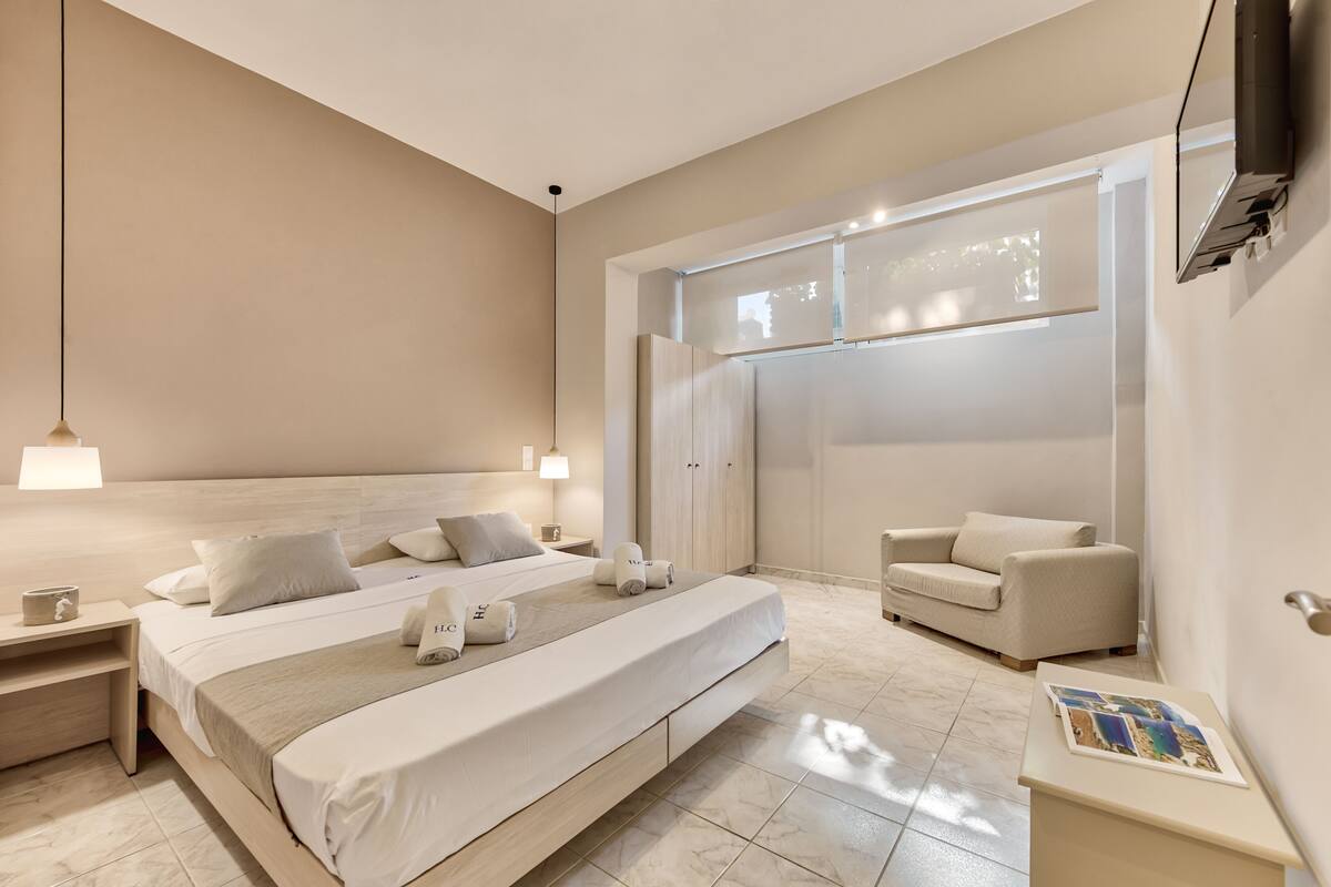 Una habitación de hotel moderna con una cama grande, mesitas de noche, un sofá y un televisor de pantalla plana montado en la pared.