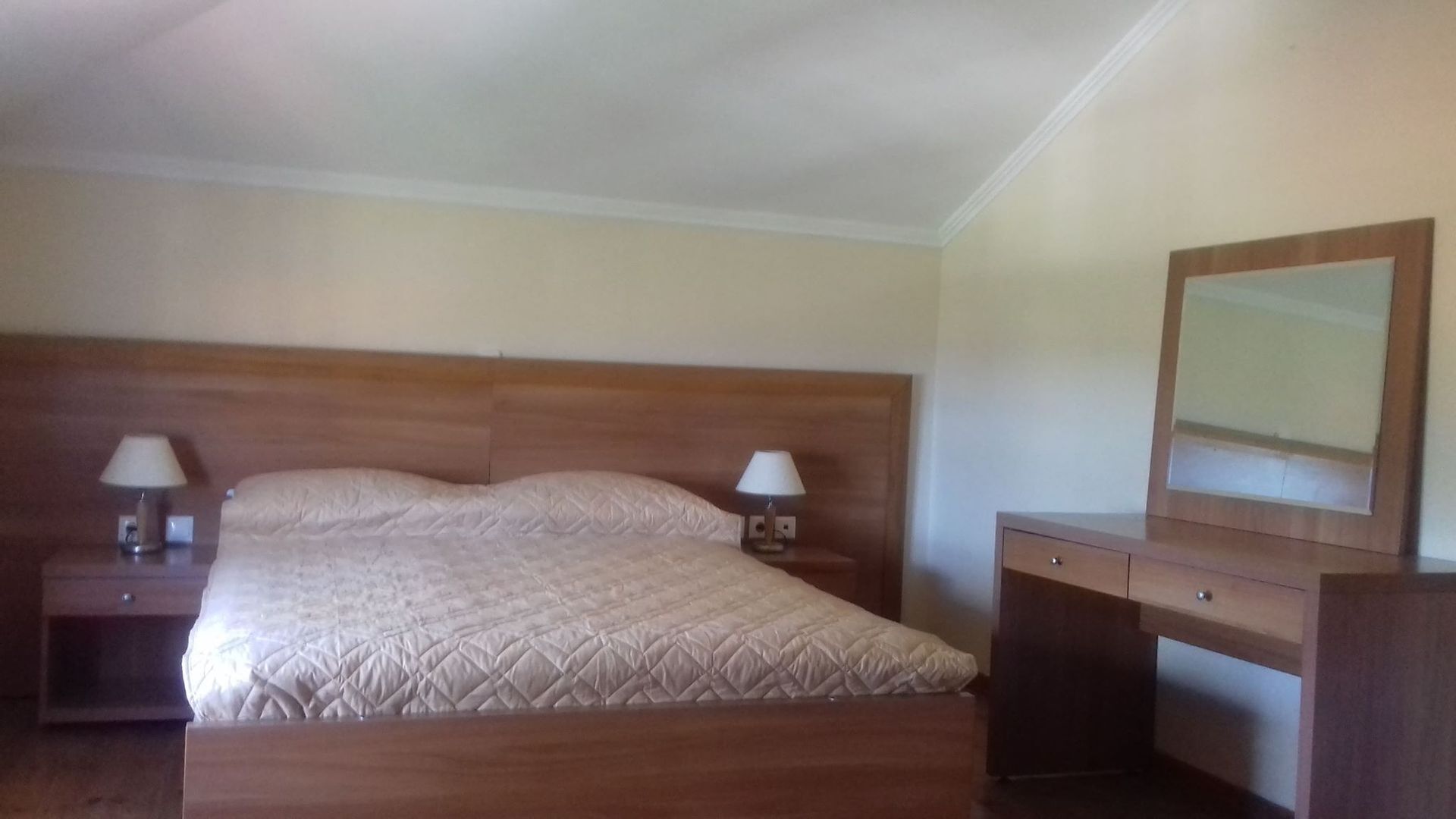Une chambre à coucher avec un lit en bois, deux tables de chevet avec des lampes, une commode et un miroir.