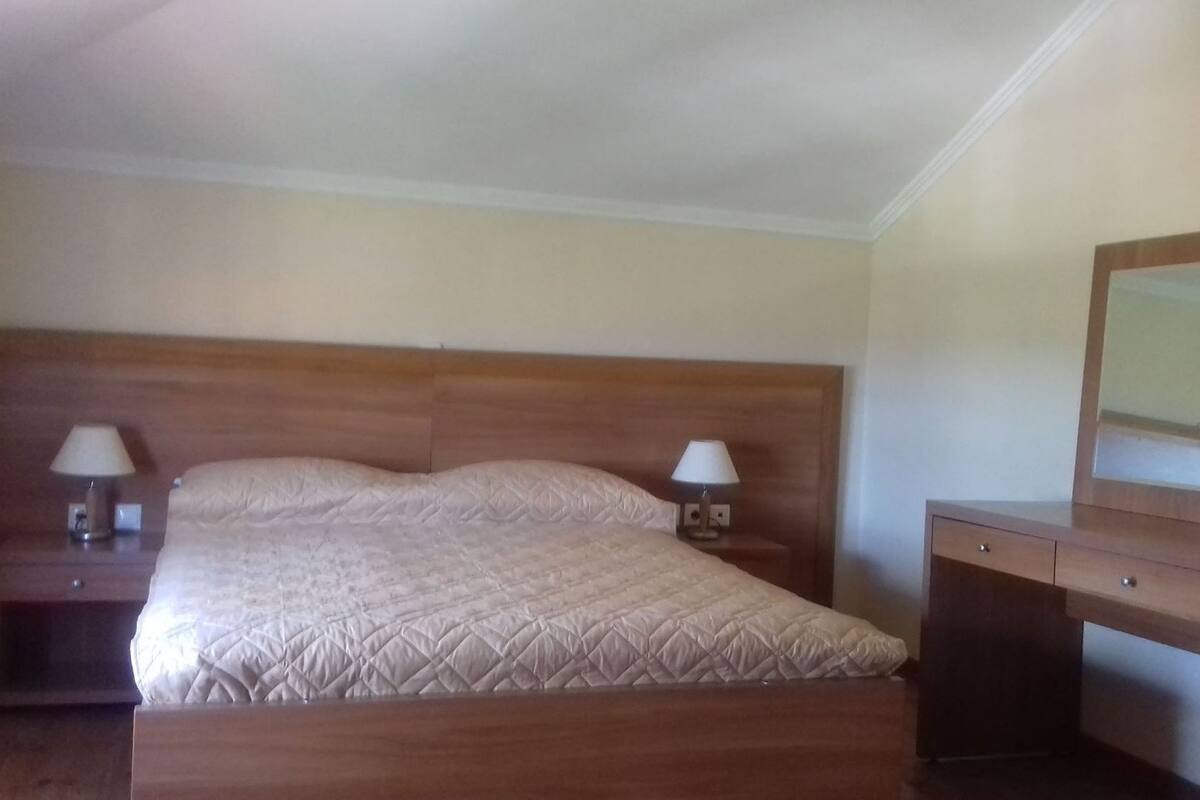 Un dormitorio con una cama de madera, dos mesitas de noche con lámparas, un aparador y un espejo.