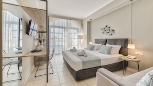 A modern hotel room with a large bed, a desk, a chair, a TV, and a view of the outdoors.