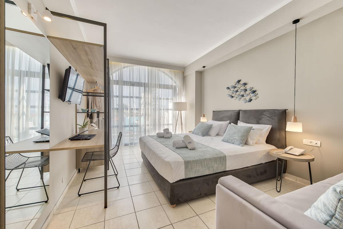 Una habitación de hotel moderna con una cama grande, un escritorio, una silla, un televisor y vistas al exterior.