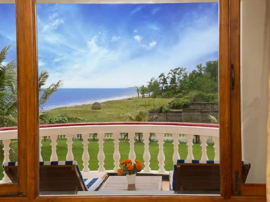 A balcony with a view of the ocean and a grassy area with trees.