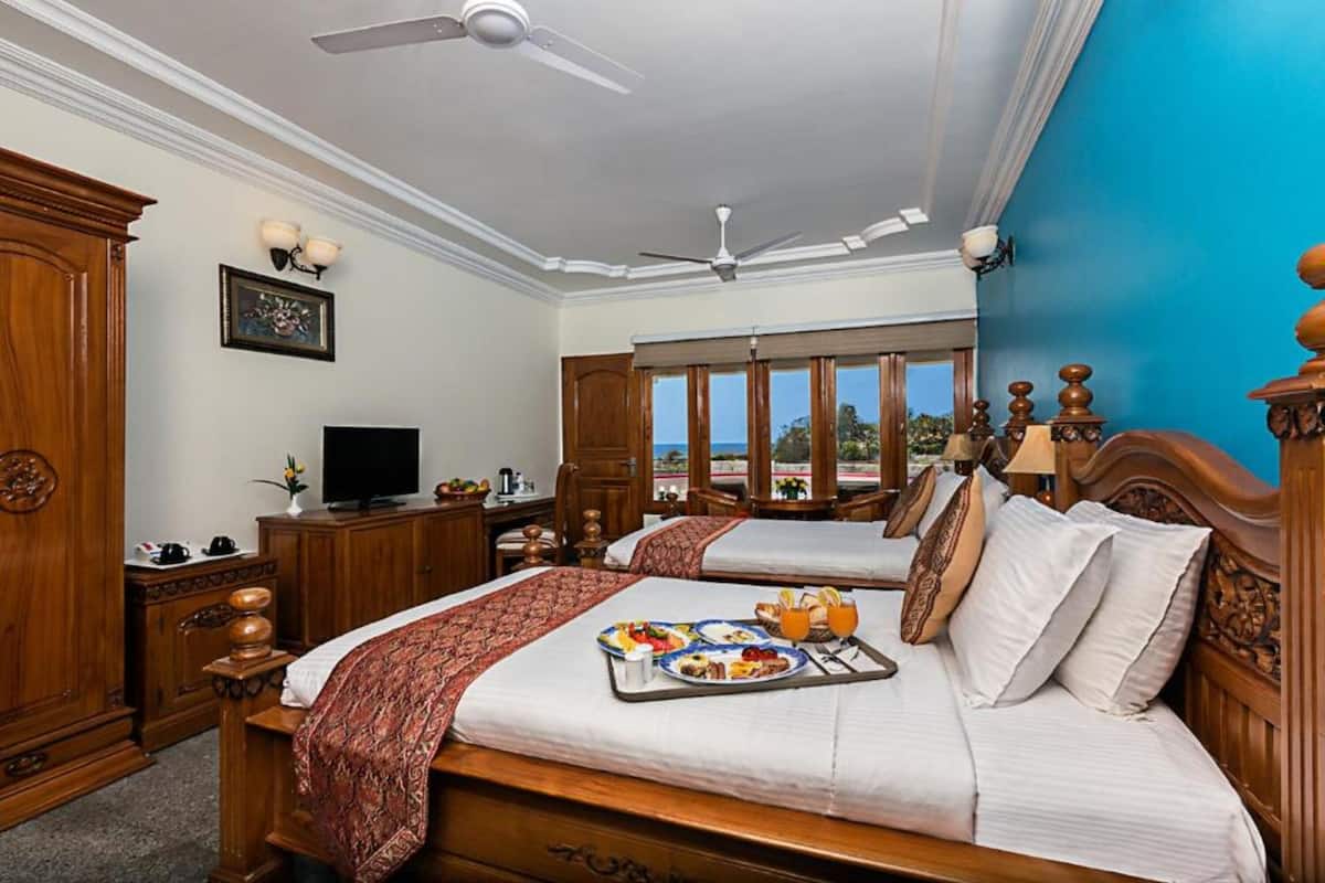 Habitación de hotel con dos camas, televisión, escritorio con lámpara y vista al exterior.