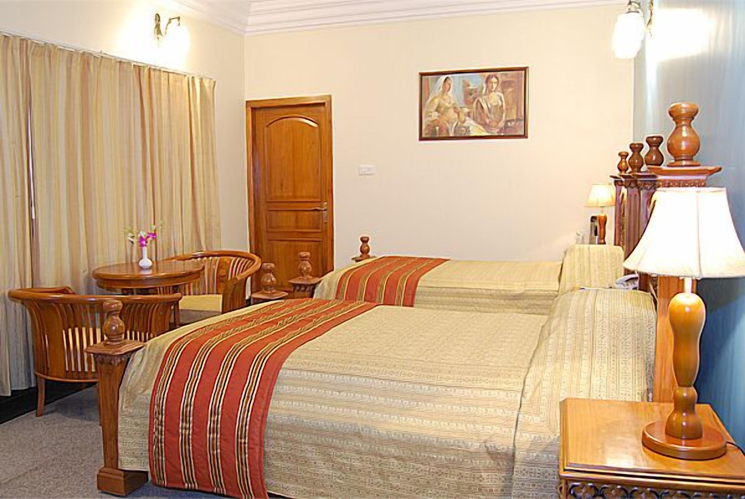 A hotel room with two beds, a wooden chair, a small table, and a lamp.