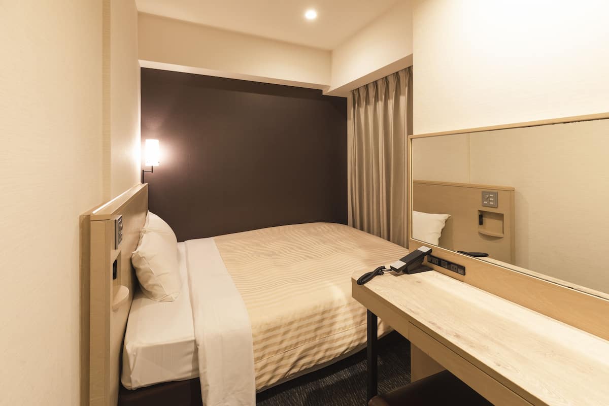 A hotel room with a bed, bedside table, and a mirror.