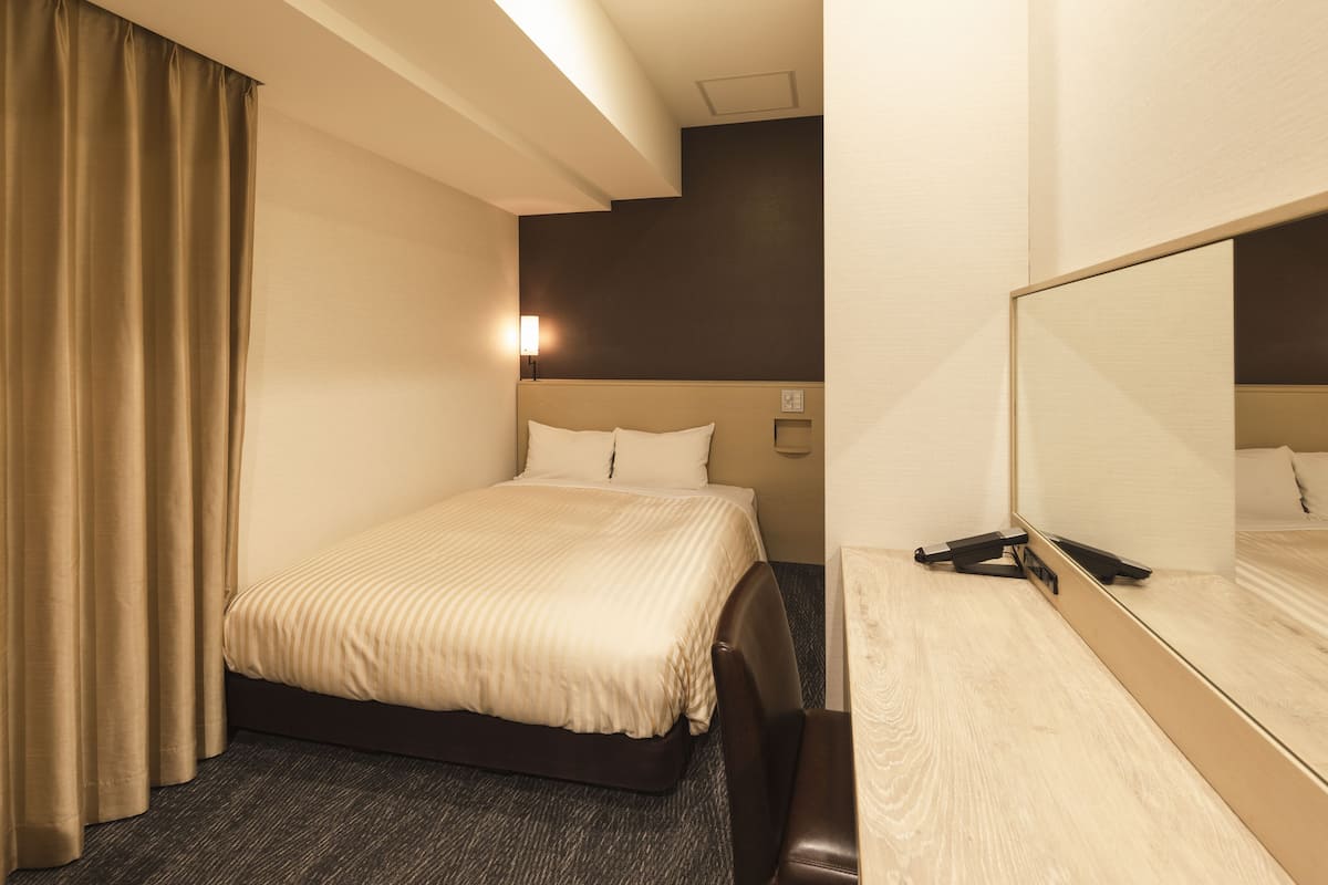 A hotel room with a bed, a desk, and a mirror.