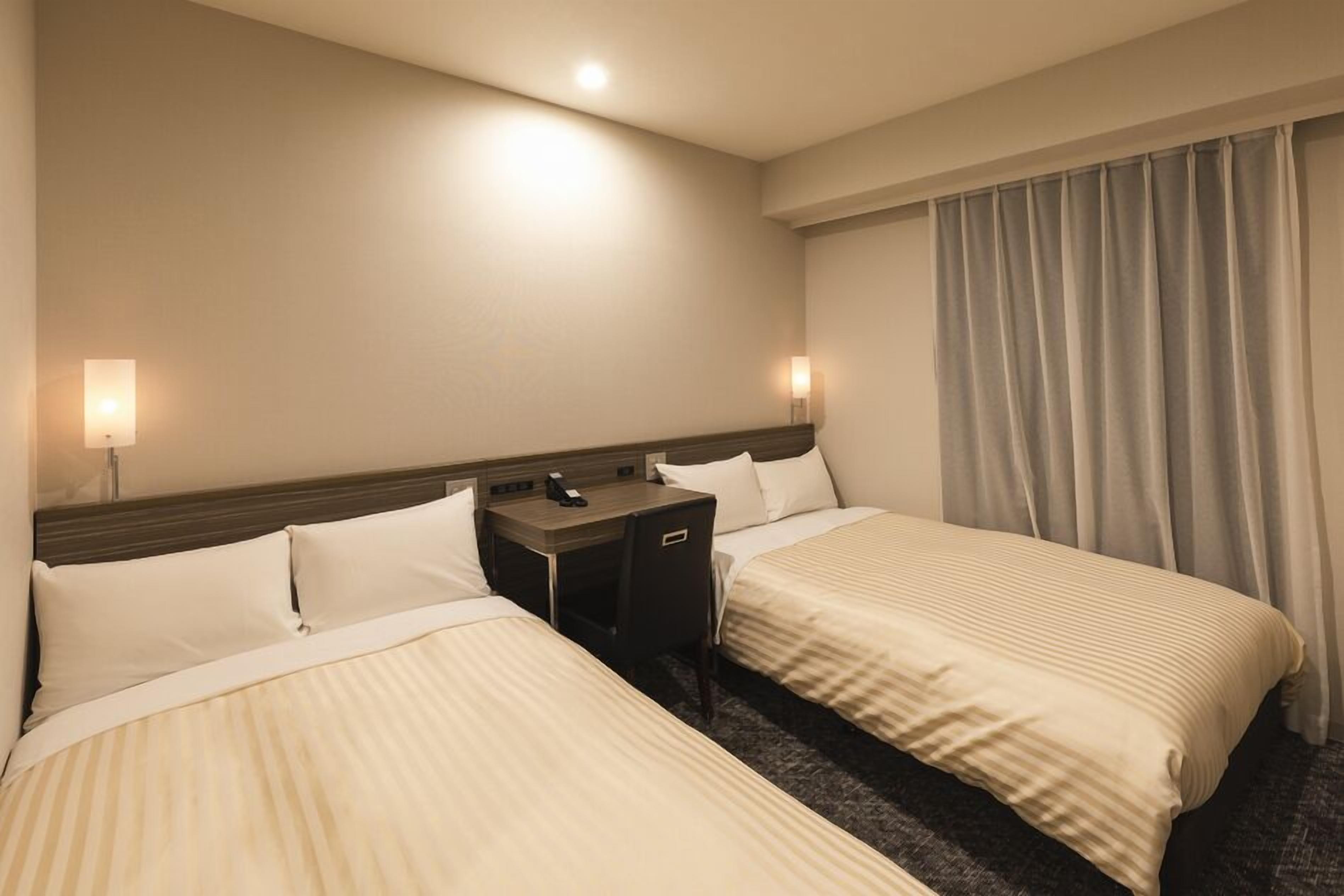 Quarto de hotel com duas camas, uma escrivaninha e uma mesinha de cabeceira.