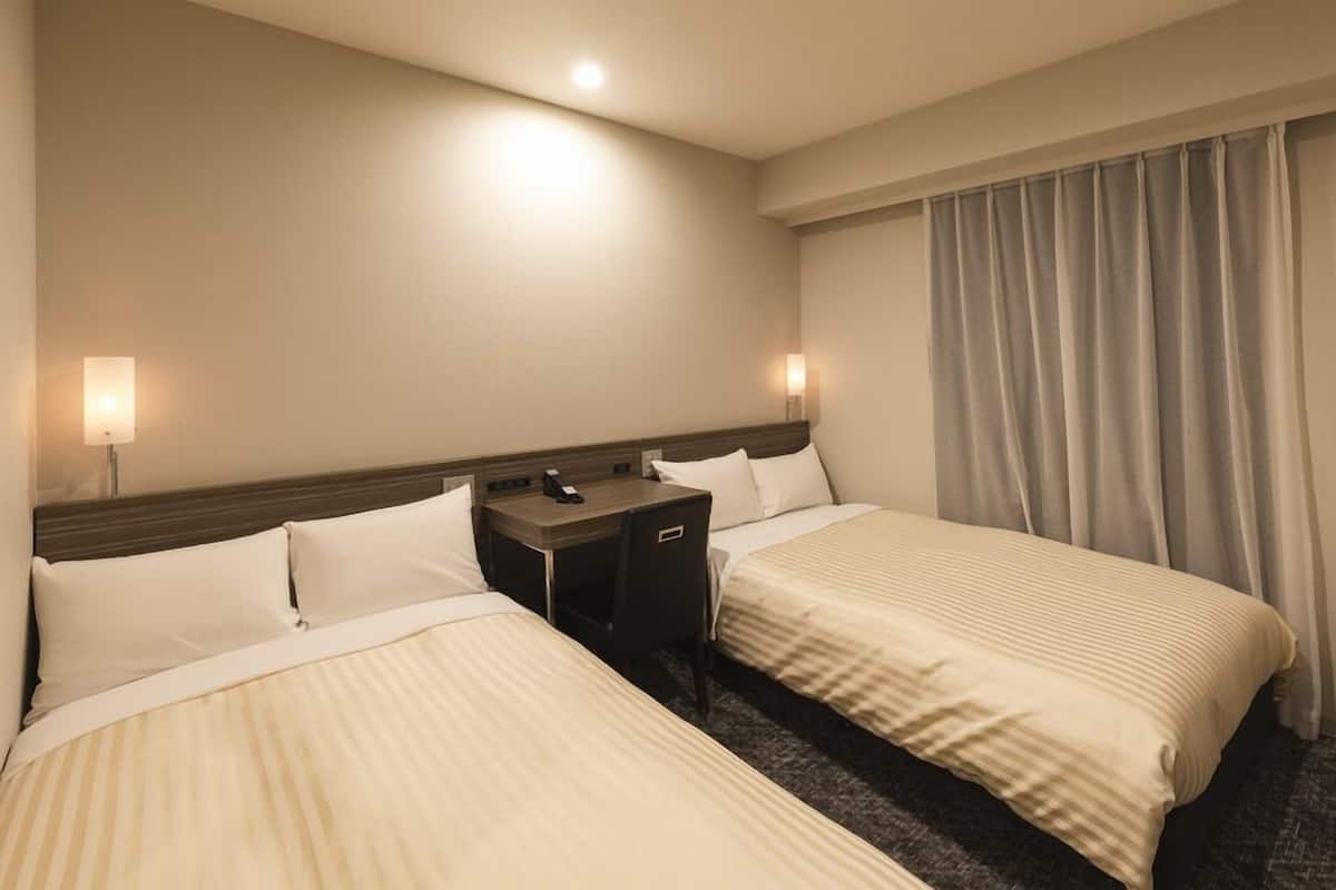 Quarto de hotel com duas camas, uma escrivaninha e uma mesinha de cabeceira.