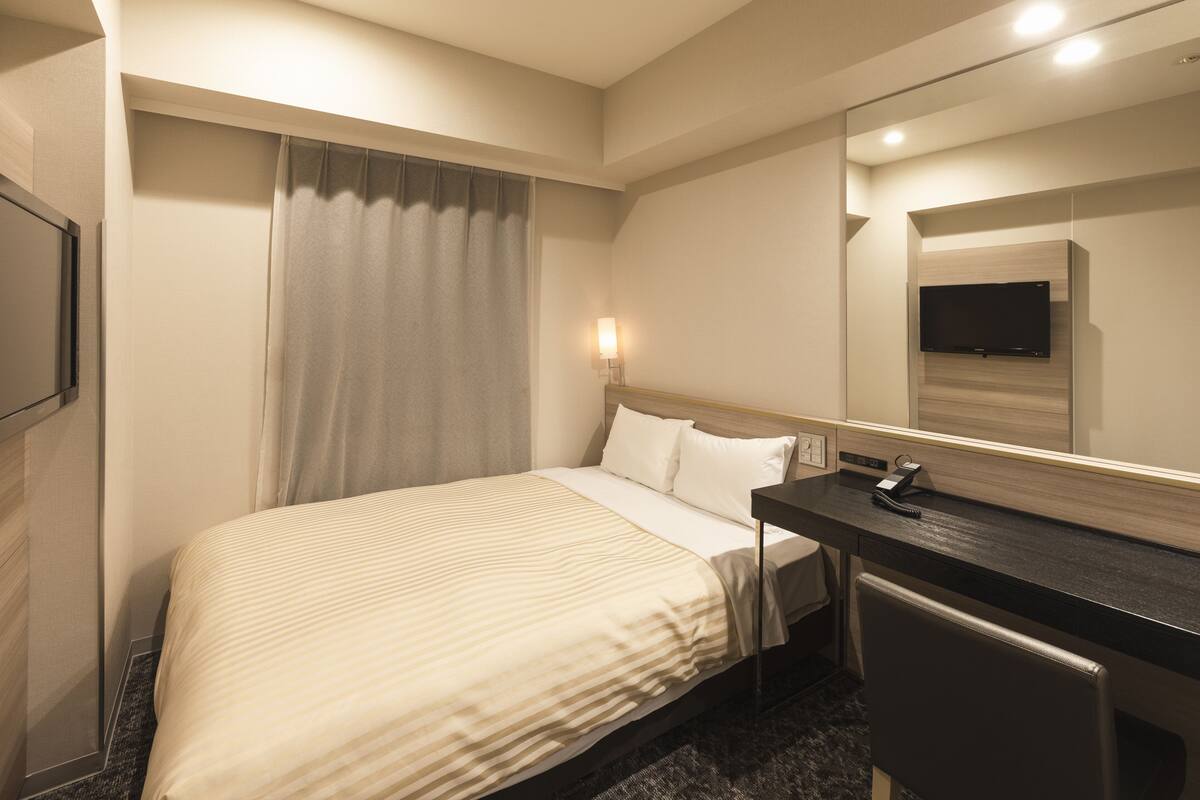 A hotel room with a bed, a desk, a mirror, and a television.