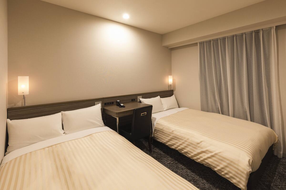 A hotel room with two beds, a nightstand, a desk, and a lamp.
