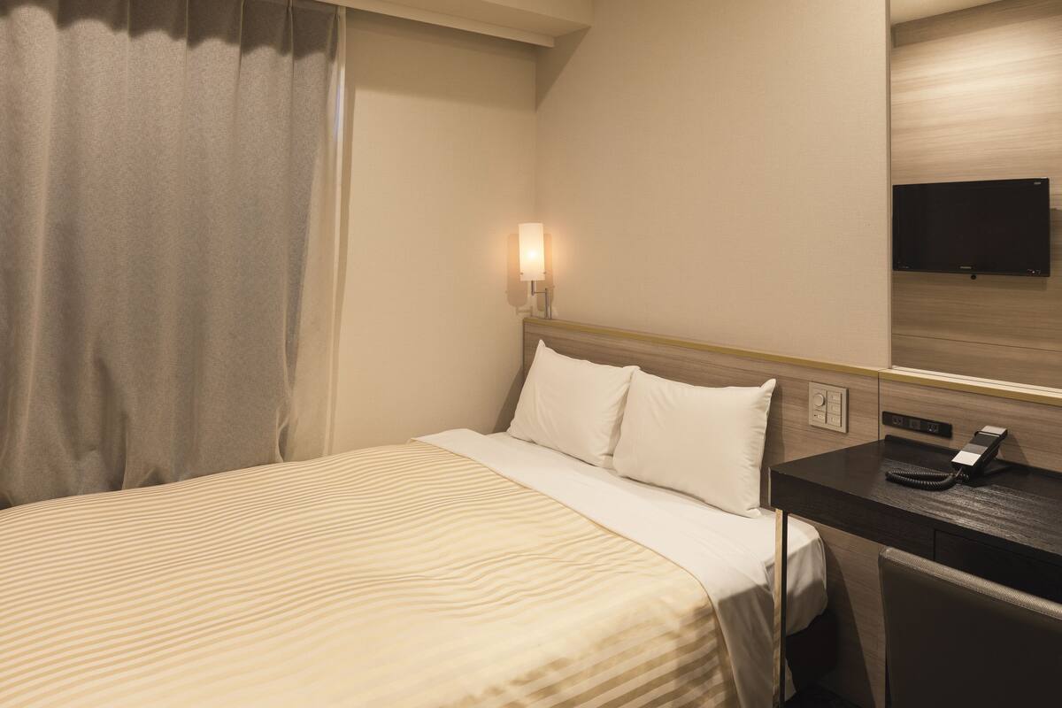 A hotel room with a bed, a desk with a telephone, and a wall-mounted television.