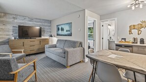 A modern living room with a grey sofa, wooden chairs, a flat-screen TV, and a dining table. - Lamphouse By Basecamp (Canmore)